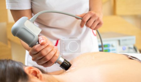 Photo for Close up of extracorporeal shockwave therapy in beauty salon. Physical therapy for neck and back muscles,spine with shock waves. Young woman wearing protective mask during treatment in salon. - Royalty Free Image