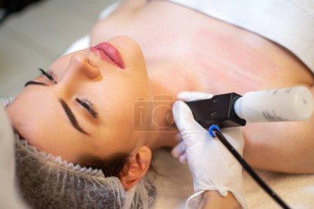 Schönheitsärztin mit Ultraschall-Scraber bei der Ultraschallreinigung des Halses weiblicher Klienten.