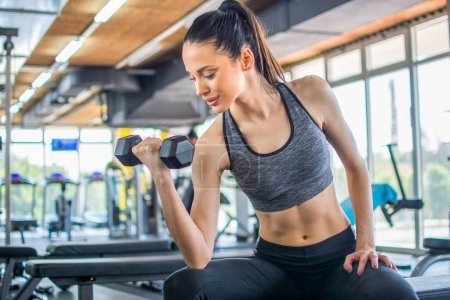 Photo for Beautiful young sportswoman lifting weights and working on her biceps in a gym - Royalty Free Image