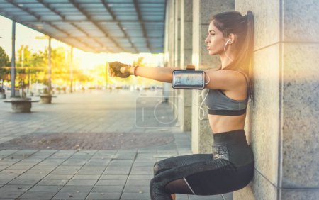 Photo for Young sportswoman doing squats against wall outdoors - Royalty Free Image