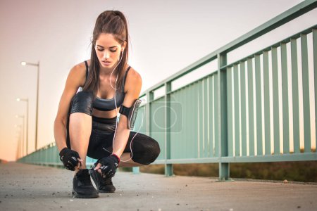 Téléchargez les photos : Sporty jeune femme attachant lacets de chaussures à l'extérieur. - en image libre de droit
