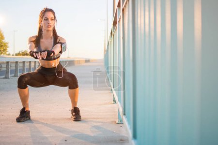Téléchargez les photos : Femme sportive faisant squats sur une route au coucher du soleil - en image libre de droit