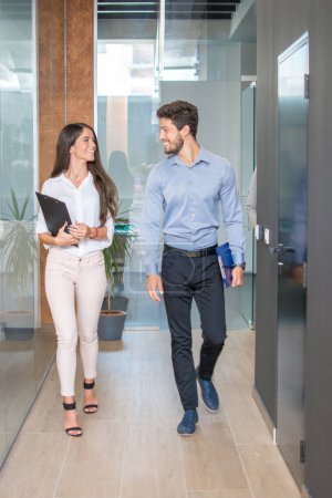 Photo for Smiling business people walking through office hallway. - Royalty Free Image