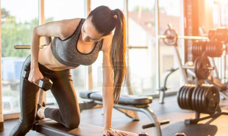 Photo for Active sporty woman flexing muscles with dumbbell at gym - Royalty Free Image