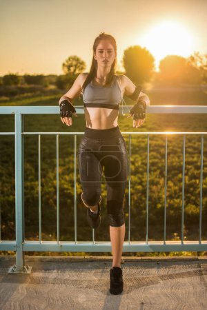 Téléchargez les photos : Femme sportive penchée sur les ponts clôture à l'extérieur pendant le coucher du soleil. - en image libre de droit