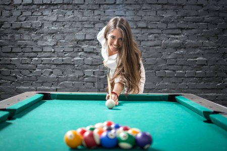 Happy business woman playing a game of billiards and preparing to break pyramid of balls on the pool table