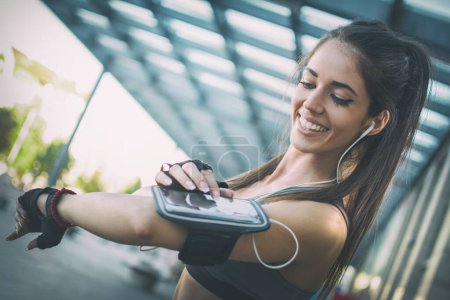Téléchargez les photos : Portrait de fille sportive souriante utilisant une application de fitness pour téléphones intelligents sur le brassard - en image libre de droit
