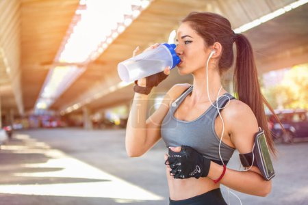Téléchargez les photos : Sportswoman boire de l'eau après la formation sportive en plein air - en image libre de droit