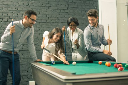 Hombres y mujeres jóvenes jugando billar en la oficina después del trabajo
