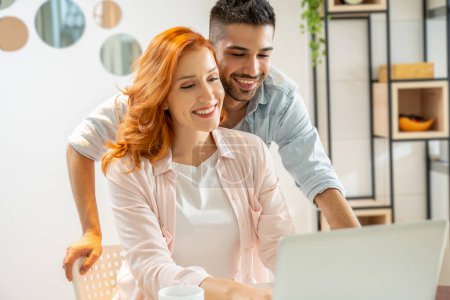 Photo for Happy couple surfing on the internet and relaxing together at home. Young man and ginger woman have fun shopping online together on computer. - Royalty Free Image