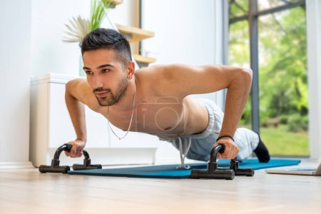Téléchargez les photos : Heureux jeune homme beau faire pousser vers le haut exercice avec des équipements à la maison - en image libre de droit