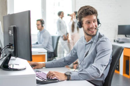 Foto de Sonriente agente de operador de atención al cliente guapo con dispositivo manos libres trabajando en el centro de llamadas. - Imagen libre de derechos