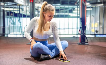 Photo for Young sporty woman listening to music in gym. Attractive blonde woman taking a break in a gym. - Royalty Free Image