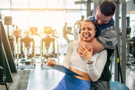 Photo for Muscular fit man choking a young female personal trainer with his arm muscle at the gym. Friends having fun at the gym. - Royalty Free Image
