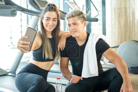 Téléchargez les photos : Couple sportif faisant selfie photo pour les médias sociaux sur le téléphone intelligent pendant la pause d'exercice au gymnase. - en image libre de droit
