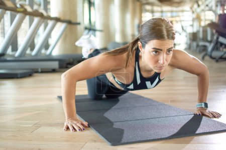 Téléchargez les photos : Jeune femme sportive faisant push-ups genou sur tapis d'exercice à la salle de gym - en image libre de droit