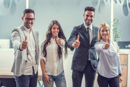Foto de Gente de negocios feliz mostrando pulgares hacia arriba mientras está de pie en la oficina. - Imagen libre de derechos