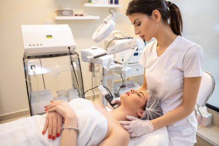 Foto de Paciente femenina que disfruta de un procedimiento de rejuvenecimiento realizado por un terapeuta en una clínica de belleza - Imagen libre de derechos