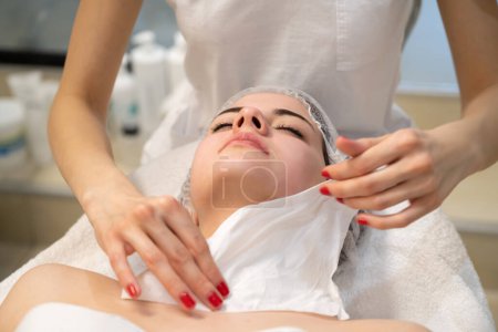 Foto de Terapeuta femenina que limpia la cara de la joven con papel después del tratamiento de la piel en el salón de belleza del spa. - Imagen libre de derechos