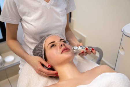 Young female patient getting radio frequency lifting on her face in beaut salon.