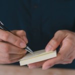 businessman hand using pen and sticky note or post it to writing a message memorendum