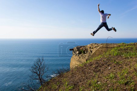 Photo for Fearless man jumps high in the air by cliff edge on sunny day. Adventure traveler. Entrepreneur success, no fear, dare concept - Royalty Free Image