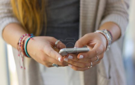 Téléchargez les photos : Téléphone portable sur les mains d'une adolescente blonde avec des ongles peints, des bracelets et des anneaux. génération millénaire, médias sociaux, concept de dépendance smartphone - en image libre de droit
