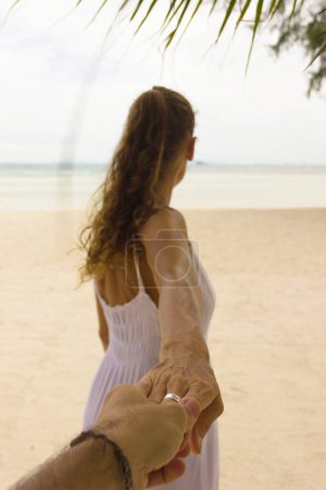 Téléchargez les photos : Irresistible woman on white dress with long, brown hair and silver ring on the beach invites her couple to follow her. Invitation, temptation, holidays concepts. - en image libre de droit