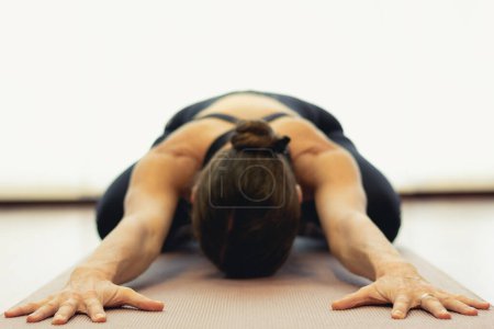 Foto de Yogi woman practices child pose in bright studio. Focus on hands of lady in balasana on pink mat. Healthy lifestyle, resting exercise, workout, sportswear, yin yoga concepts. Vintage effect applied - Imagen libre de derechos