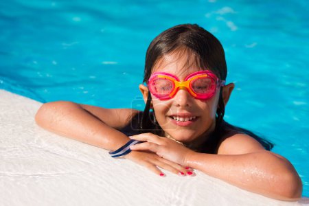 Téléchargez les photos : Petite fille avec des lunettes roses souriant au bord de la piscine. Vacances d'été, bracelet d'hôtel tout compris, bracelet, sous-marin, tuba, vacances de voyage, station familiale, plaisir, concepts de bonheur - en image libre de droit