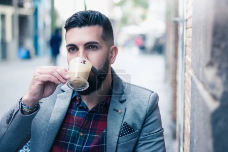 Photo for Young hipster sipping cappuccino on street cafe terrace. Elegant male model with class having cup of coffee in the city. Nicely dressed man enjoying espresso in old town Las Palmas, Spain - Royalty Free Image