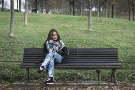 Foto de Mujer joven sentada en el banco del parque mirando hacia el espacio a su lado. Falta alguien, conceptos rotos del corazón - Imagen libre de derechos