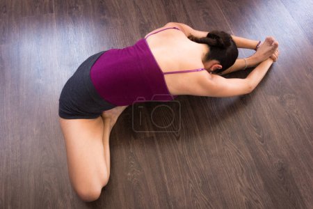 Foto de Woman in janu sirsasana from top on wood planks floor. Female yogi on head to knee forward bend. Lady practices yoga. Sitting posture, spinal twist, stretching concepts - Imagen libre de derechos