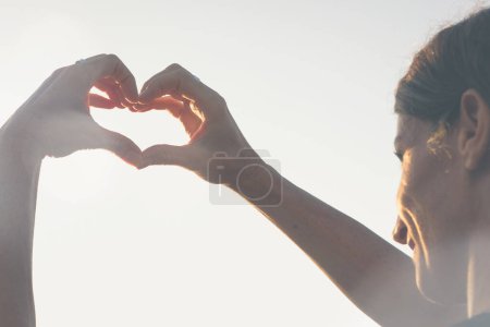 Photo for Woman with hands in heart shape on sunny day. Young lady with romantic symbol at twilight. Valentine Day, sunny, healthy lifestyle concepts - Royalty Free Image