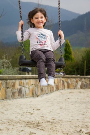 Téléchargez les photos : Belle petite fille qui s'amuse sur le swing à l'aire de jeux de Bilbao - en image libre de droit