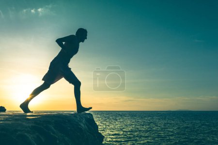 Téléchargez les photos : Man on the edge of a cliff about to jump into the sea on sunset in Koh Phangan island, Thailand. No fear concept. Vintage effect. - en image libre de droit