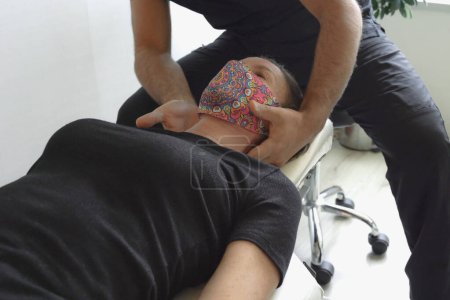 Téléchargez les photos : Patiente avec masque facial couchée sur civière tandis que l'ostéopathe masse son cou. Physiothérapie, concepts d'ajustement des vertèbres - en image libre de droit