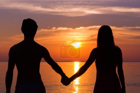 Foto de Romantic Valentine's Day scene of a young couple silhouettes holding hands by the sea staring at colorful sunset in the island of Koh Phangan, Thailand. Honeymoon destination, love concept - Imagen libre de derechos