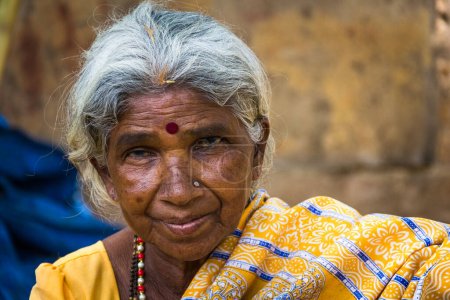 Portrait of Indian elder lady with traditional bindi as a third eye, piercing on nose and wearing a yellow saree in Mysore, Karnataka, India. Close up on Indian ethnicity old woman