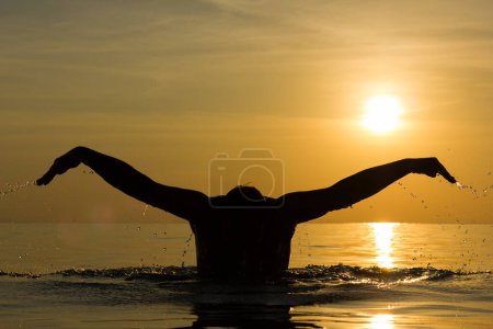 Téléchargez les photos : Silhouette of man swimming butterfly stroke technique at splendid colorful sunset on the beach in the island of Koh Phangan, Thailand - en image libre de droit