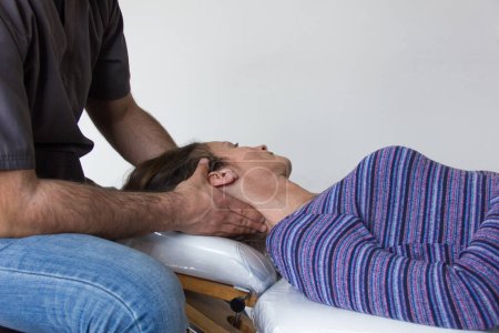 Foto de Osteopath treats female patient injury on neck lying on white stretcher. Doctor examines young woman - Imagen libre de derechos