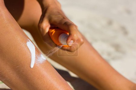 Téléchargez les photos : Close up on woman's upper arm and hand spreading sun cream at the beach on a hot, sunny day. Tanning, sunblock spread, skin care, ultraviolet rays protection, cancer prevention concept - en image libre de droit