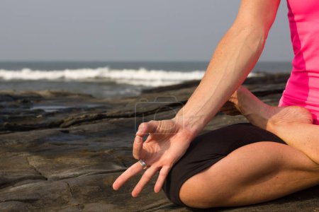 Foto de Close up of a woman's hand while practicing yoga and meditation on the rocks by the sea in Vagator Beach, Goa, India. Yogi on the beach, peaceful mindfulness concept - Imagen libre de derechos