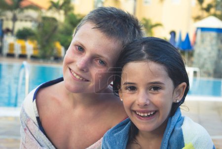 Foto de Couple of kids portrait smiling wrapped up in towels by swimming pool - Imagen libre de derechos