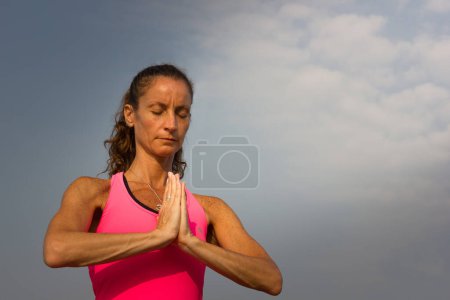 Téléchargez les photos : Femme méditant avec les mains ensemble sur la plage à Goa avec le ciel bleu sur le fond. Concept de moment paisible, concentré, zen - en image libre de droit