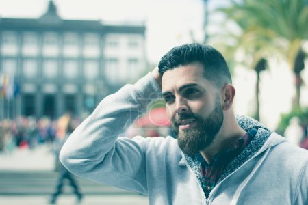 Photo for Handsome model boasting his new haircut outdoors. Young hipster with full beard doing his hair with style. Man with hand on head on sunny day in the city - Royalty Free Image
