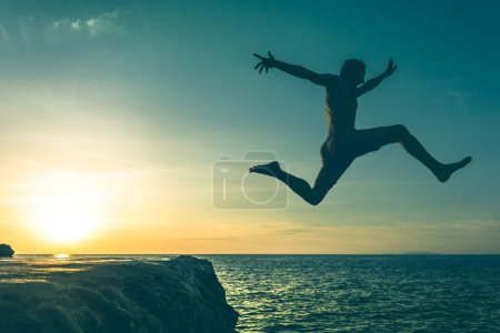 Foto de Man jumping over a cliff into the sea on sunset in Koh Phangan island, Thailand. Vintage effect. No fear, courage, brave, dare concept - Imagen libre de derechos