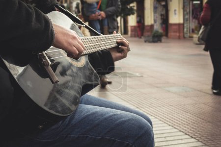 Foto de Manos de joven tocando la guitarra negra en la calle mientras los peatones pasan por La Serena en el centro de Chile - Imagen libre de derechos