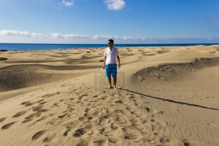 Photo for Young man walking on Maspalomas sand dunes in Gran Canaria. Lonely tourist on arid landscape with sea on the background in Canary Islands, Spain. Summer holidays, travel destination concepts - Royalty Free Image