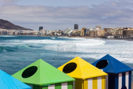 Foto de Coloridos contenedores de reciclaje con la playa de Las Canteras y la ciudad de Las Palmas en el fondo en España. Día soleado en la isla de Gran Canaria. Conservación ambiental, concepto limpio - Imagen libre de derechos